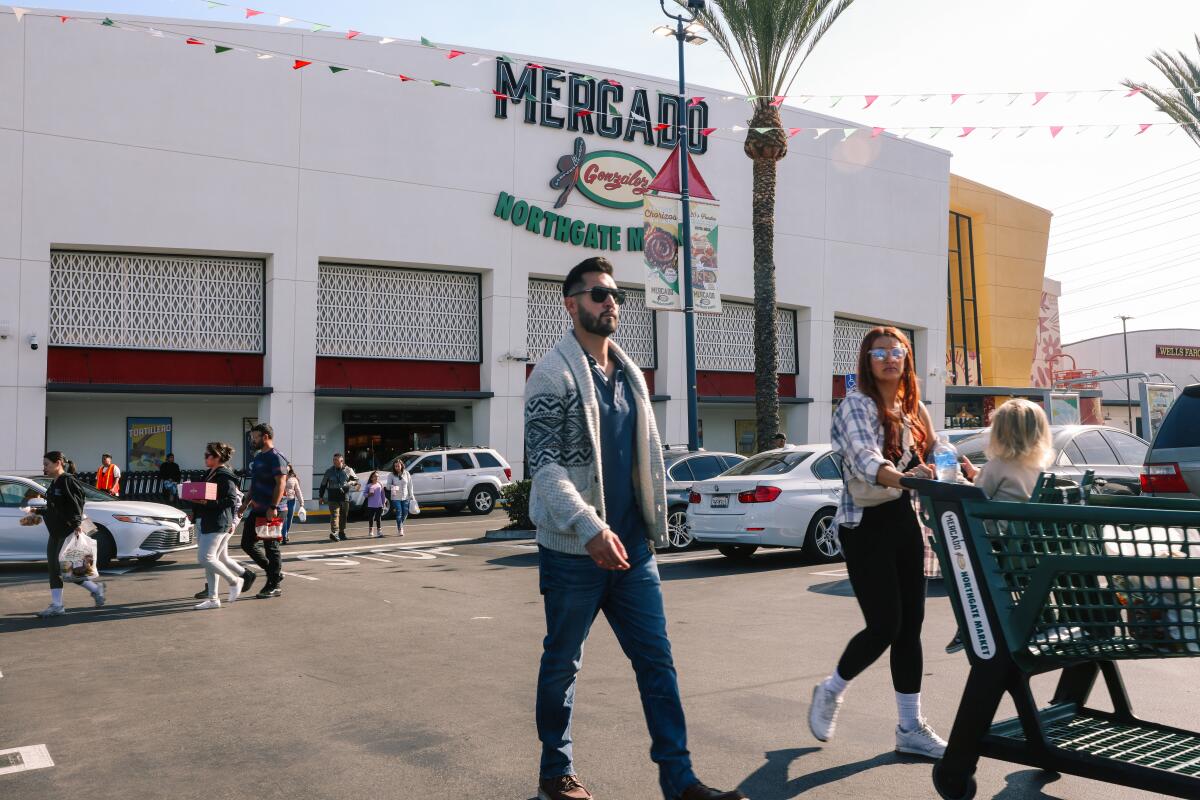 Ein Außenfoto von Menschen, die auf einem Parkplatz vor dem Mercado González Northgate Market herumlaufen.