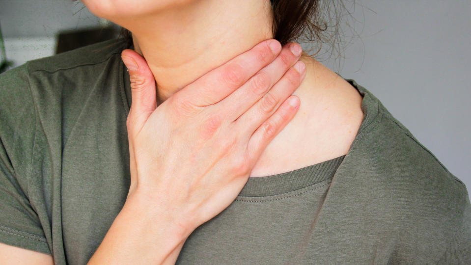 Eine Frau in den Wechseljahren fasst sich wegen Hitzewallungen an den Hals. (Foto über Getty Images)