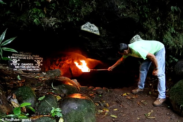 Besucher der Höhle des Todes demonstrieren ihre Wirksamkeit, indem sie eine brennende Fackel an den Eingang halten.  Beachten Sie das Warnschild mit tödlichen Totenköpfen und gekreuzten Knochen, auf dem steht: „Gefahr!“  Kein Durchgang ab hier'