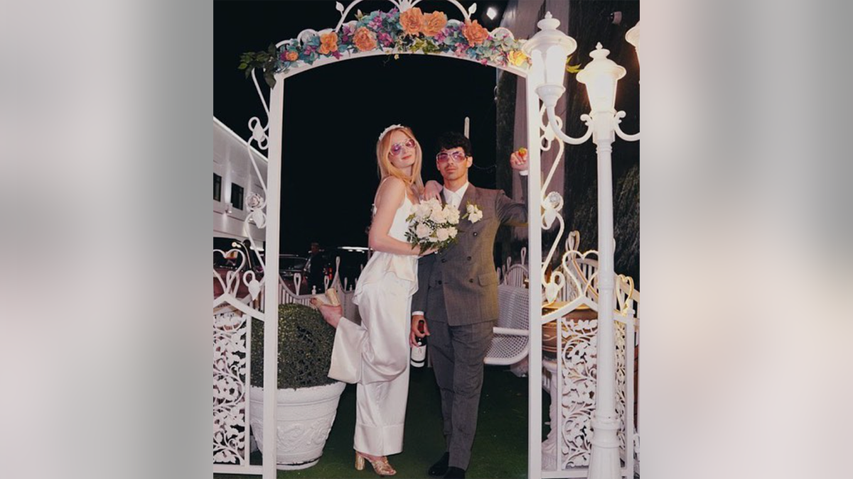 Sophie Turner zeigt ihren Fuß in einem weißen Overall unter einem Bogen mit Joe Jonas bei ihrer Hochzeit in Las Vegas