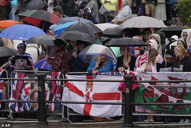 Royal fans shelter under umbrellas as rain falls while they wait for the parade in London today