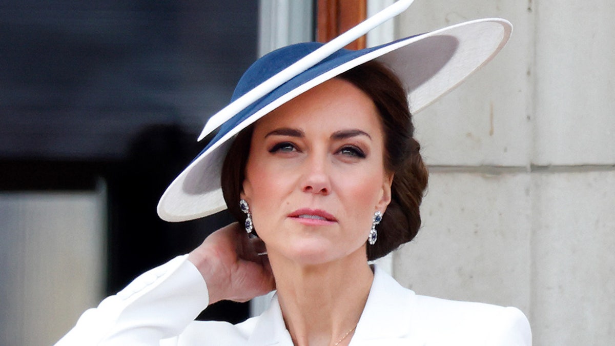 Eine Nahaufnahme von Kate Middleton mit einem gestreiften blau-weißen Hut und einem passenden weißen Kleid
