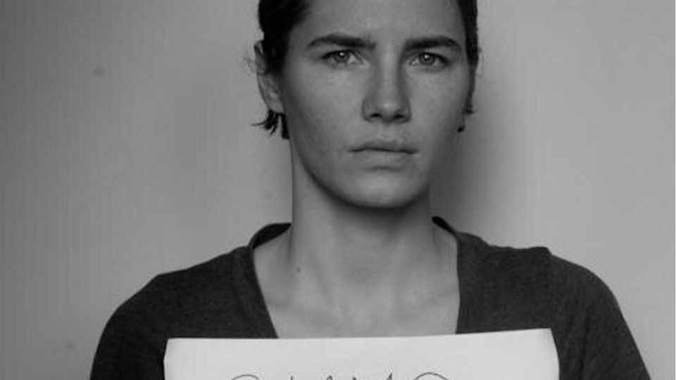 Amanda Knox holds a poster that reads "Siamo innocenti" into the camera
