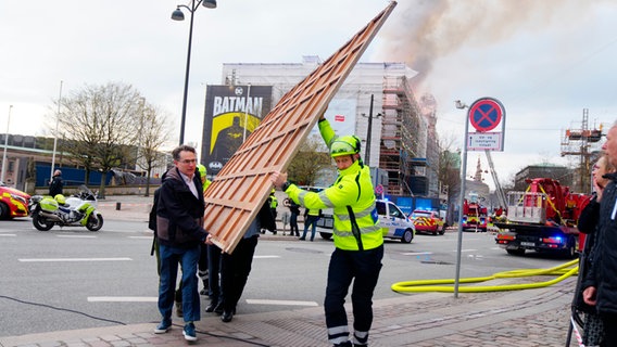 A firefighter and several helpers carry a painting across a street.  © picture alliance Photo: Ida Marie Odgaard