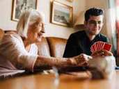 A senior woman and a young man play cards together.