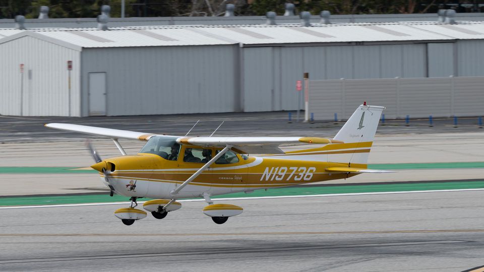 A Cessna 172 painted gold yellow and white flies low over a runway