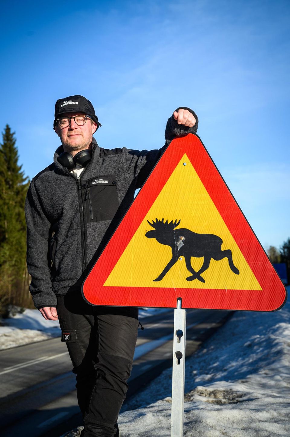 Johan Erhag, Miterfinder und Projektleiter der Elch-Show in Schweden, mit einem Straßenschild, das vor Elchen warnt
