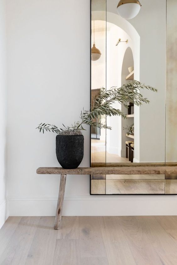 A large mirror and a wooden bench to enhance the white wall