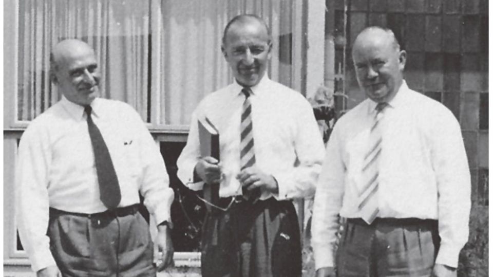 Black and white image: Three men stand next to each other