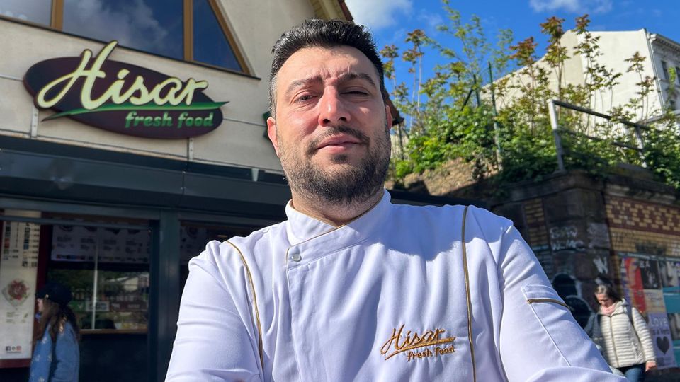 Snack bar operator Arif Keles stands in front of his kebab shop in a white chef's jacket