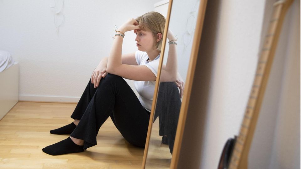 Woman sits next to mirror and looks depressed