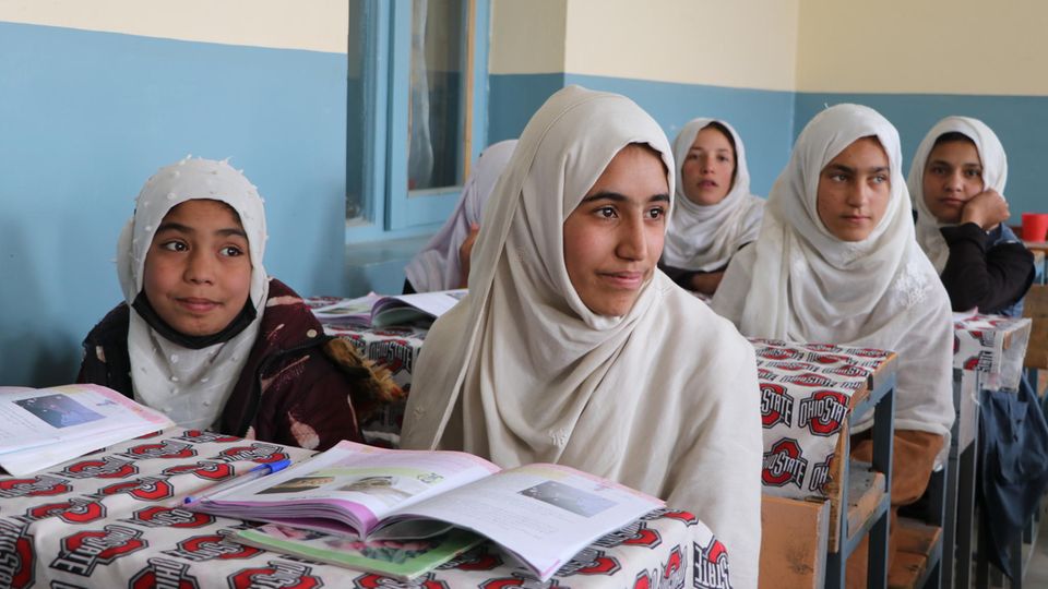 Two Afghan girls with white headscarves sit at each of three tables.