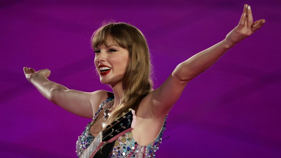 Taylor Swift stretches her arms in the air at a concert