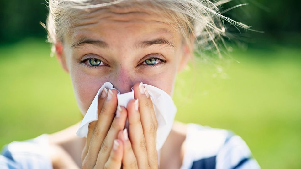 Young girl with allergy stands outside on a meadow and blows her nose into a tissue.