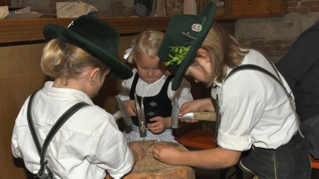 Trostberg: At the church fair in Trostberg, two boys in traditional costume with long hair hammer nails into a tree stump.  You can also see a son of the Heigermoser family (left).