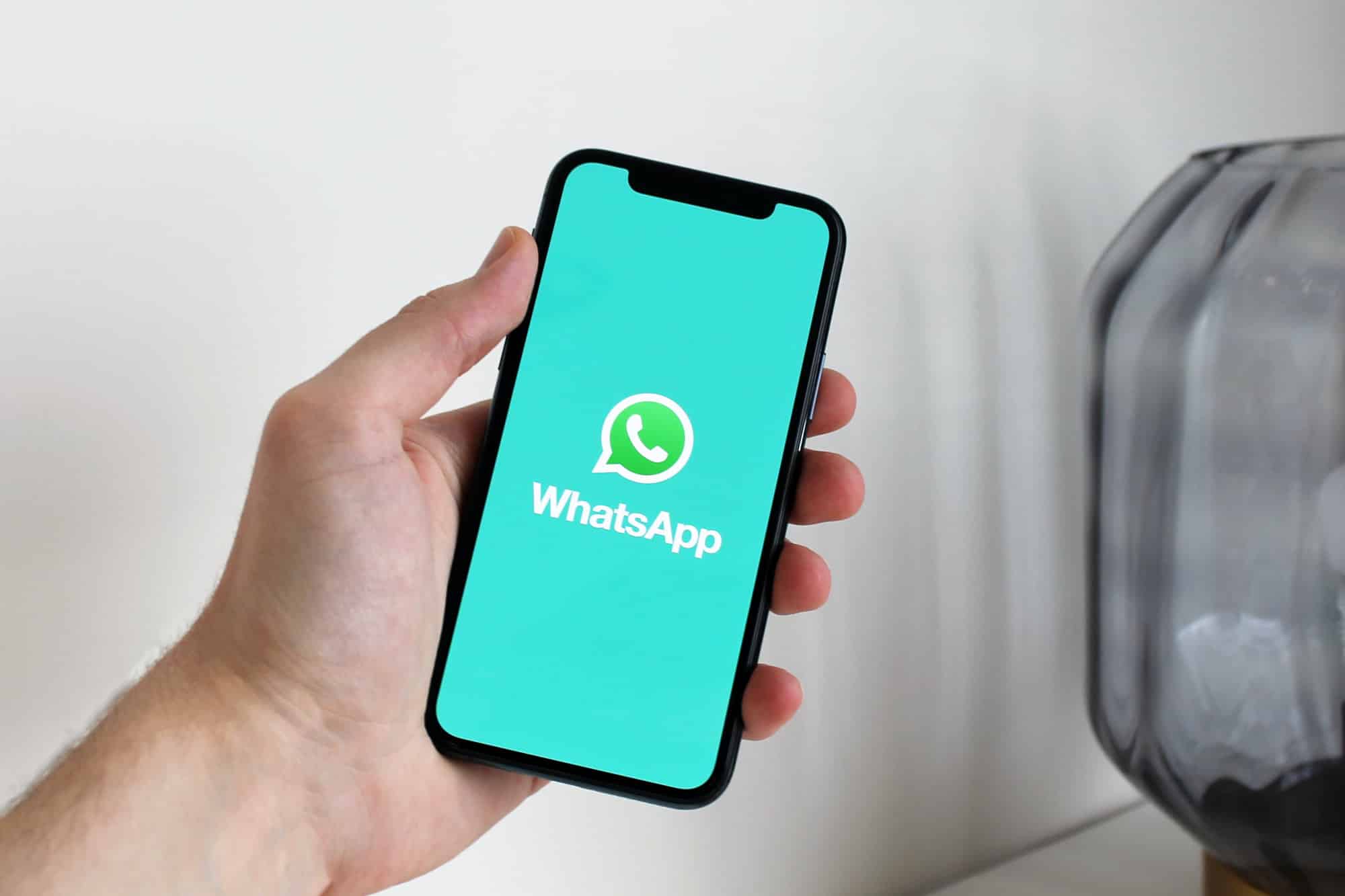 A person holds an iPhone with a green screen showing the WhatsApp logo