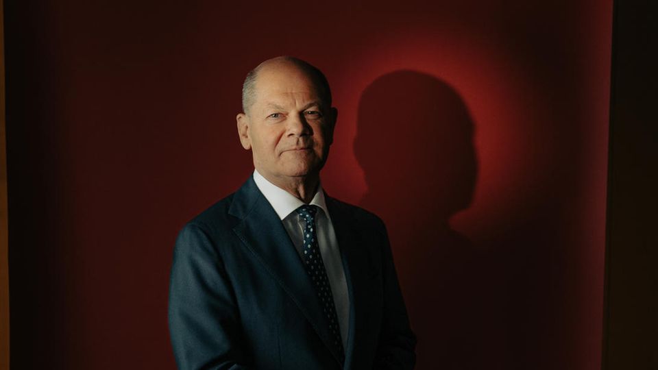 Portrait of Olaf Scholz in front of a red background with folded hands