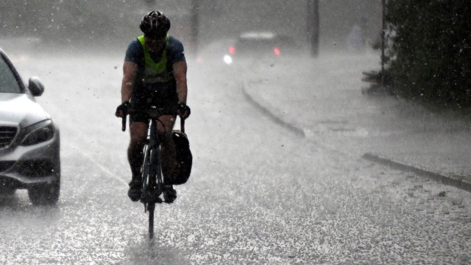 Weather extremes on 02.05.2024, North Rhine-Westphalia, Cologne: A cyclist rides through a hailstorm
